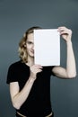 Portrait young man with a smile is holding white blank paper card covering his face, standing isolated on gray background Royalty Free Stock Photo