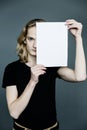 Portrait young man with a smile is holding white blank paper card covering his face, standing isolated on gray background Royalty Free Stock Photo