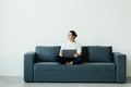 Portrait of young man smiling and using laptop while sitting on sofa at home Royalty Free Stock Photo