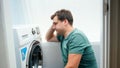 Portrait of young man struggling and getting confused while setting washing machine for laundry Royalty Free Stock Photo