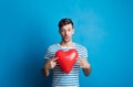 Portrait of a young man in a studio on a blue background, holding red heart. Royalty Free Stock Photo