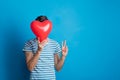 Portrait of a young man in a studio on a blue background, holding red heart. Royalty Free Stock Photo