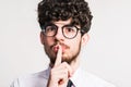 Portrait of a young man in a studio, finger in front of his mouth. Close up.