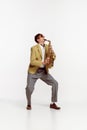 Portrait of young man in stylish yellow jacket playing saxophone isolated over white background. Jazz performer Royalty Free Stock Photo
