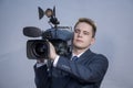 Portrait of a young man in a suit, who stands holding a TV camera on his shoulder on a light background. The operator works with