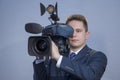 Portrait of a young man in a suit, who stands holding a TV camera on his shoulder on a light background. The operator works with