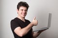 Young man in t shirt standing against textured wall with copy space for ads, holding laptop and looking at camera with happy smile Royalty Free Stock Photo