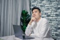 Portrait of young man thinking while serious working at home with laptop on desk