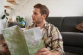 Portrait of young man, traveller, sitting packing suitcase, looking at travel map, choosing holiday destination Royalty Free Stock Photo