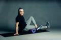 Portrait of a young man with an unusual hairstyle of mohawk from blue braids in sportswear doing leg exercise, by dint of roller Royalty Free Stock Photo