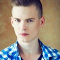 Portrait of a young man with very handsome face in blue casual shirt with stylish haircut posing over golden brown background. Royalty Free Stock Photo