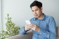 Portrait of young man wearing blue shirt looking with smartphone and sitting at his sofa in the office Royalty Free Stock Photo