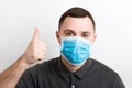 Portrait of young man wearing a medical mask at white background. Person is happy because he is finally healthy. Coronavirus