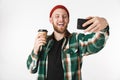 Portrait of young man wearing plaid shirt holding paper cup with coffee and using mobile phone, while standing isolated over white Royalty Free Stock Photo
