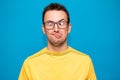 Portrait of young man wearing yellow shirt and trendy nerd glasses isolated over blue with confused face and funny expression Royalty Free Stock Photo