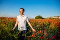 Portrait of young man in white polo standing in blooming red poppy field at sunset, Smiling boy in shirt and glasses confident and Royalty Free Stock Photo