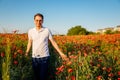 Portrait of young man in white polo standing in blooming red poppy field at sunset, Smiling boy in shirt and glasses confident and Royalty Free Stock Photo