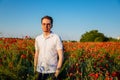 Portrait of young man in white polo standing in blooming red poppy field at sunset, Smiling boy in shirt and glasses confident and Royalty Free Stock Photo