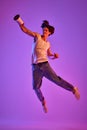 Portrait of young man in white T-shirt, singlet posing in a jump over purple background in neon light
