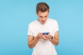 Portrait of young man in white t-shirt using cellphone with focused serious expression, addicted to mobile communication