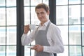 Portrait of a young man working as a professional barista, smiling at the camera and raising a cup with a coffee drink Royalty Free Stock Photo