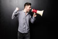 Portrait of young handsome man yelling into the megaphone over black background Royalty Free Stock Photo