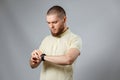 Portrait of a young man in a yellow T-shirt looks at his watch on a gray background. isolated, copyspace Royalty Free Stock Photo