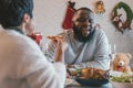 Young man with african american husband enjoying christmas lunch of turkey at decorated home with stockings, candy cane Royalty Free Stock Photo