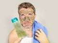 Portrait of young messy funny man in bathroom mirror with green face holding cream male beauty product applying facial mask feelin Royalty Free Stock Photo