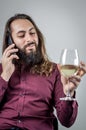 Portrait of a young Middle Eastern businessman with a beard and long hair holding a glass of white wine while having a phone conve