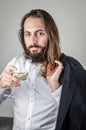 Portrait of a young middle eastern businessman with beard and long hair holding a glass of white wine and his jacket on his should Royalty Free Stock Photo