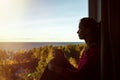 Portrait of a beautiful modern young woman sitting near a window  with a mug in hand, and watching at sea view. Royalty Free Stock Photo