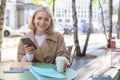 Portrait of young modern woman, student having her morning cup of coffee in city cafe, sitting outdoors, using mobile Royalty Free Stock Photo