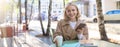 Portrait of young modern woman, student having her morning cup of coffee in city cafe, sitting outdoors, using mobile Royalty Free Stock Photo