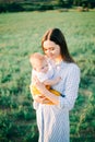 Portrait of a young mother in a blue checked dress, holding a small child in her arms,in a spacious field in the rays of the Royalty Free Stock Photo