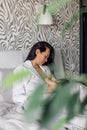 Portrait of young mother breastfeeding her daughter in bedroom, blurred green plant in foreground. Baby suckle milk and Royalty Free Stock Photo