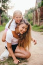 Portrait of young mother carrying her daughter on her back outdoor. Happy chilhood