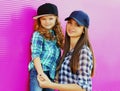 Portrait of young mother with child little girl wearing a checkered shirts and baseball cap in city over pink Royalty Free Stock Photo