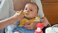 Portrait of young mother feeding her baby son setting on her laps in kitchen Royalty Free Stock Photo