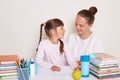 Portrait of young mother helping to write her daughter to write composition, girls looking at each other, posing isolated over Royalty Free Stock Photo
