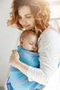 Portrait of young mother and newborn son sleeping on mother chest in blue baby sling. Family happiness vibes. Family Royalty Free Stock Photo