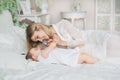 Portrait of young mother plays with her little baby on a bed