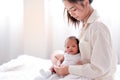 Portrait of young mother support her newborn baby on her lap and sit on bed with morning light Royalty Free Stock Photo