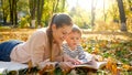 Portrait of young mother telling a story to her little son lying on yellow fallen tree leaves at autumn park Royalty Free Stock Photo