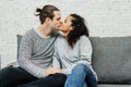 Portrait of young multiethnic couple kissing on couch at home in the living room. People, love and friendship concept Royalty Free Stock Photo