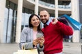 Portrait of young multiracial couple using smartphone shopping app, holding bright gift bags near city mall, outdoors Royalty Free Stock Photo