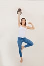 Portrait of young muscular woman wearing white top, blue jeans, standing on leg, lifting kettle bell, showing muscles. Royalty Free Stock Photo