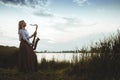 Portrait of young musician on nature background, woman playing saxophone on bank river in reeds, concept music and relax Royalty Free Stock Photo