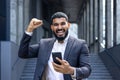 Portrait of a young Muslim businessman man standing near an office building, holding a phone in his hands and showing a Royalty Free Stock Photo