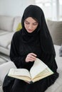 Portrait of young muslim woman reading Quran in modern home